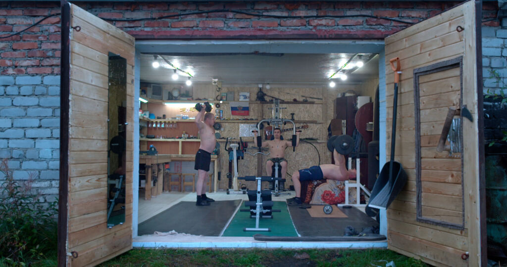 Still aus dem Dokumentarfilm "Garagenvolk". Drei Männer beim Training in einer zum Fitnessraum umgebauten Garage.