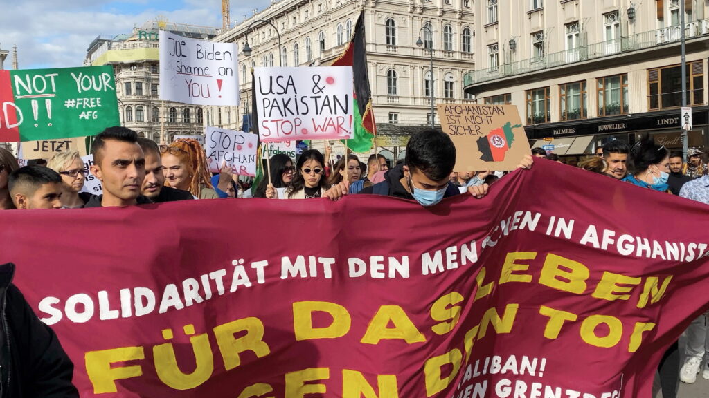 Still aus dem Dokumentarfilm "Caravan" von Lucy Ashton. Junge Männer halten ein Banner auf einer Demonstration für Solidarität mit den Menschen in Afghanistan.